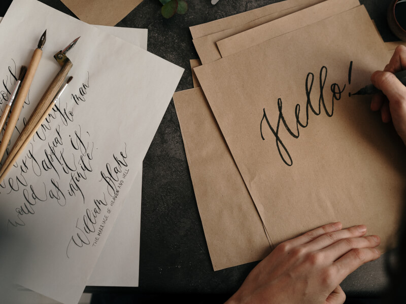 A person learning calligraphy writes hello on brown paper